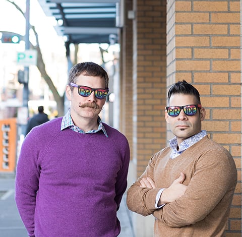 Picture of Erik and Joe outside on sidewalk. They are wearing rainbow glasses and being serious