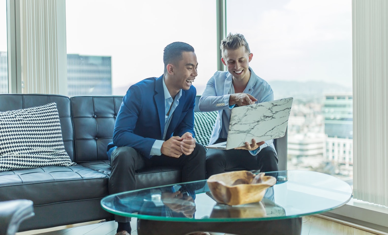 Two people sit on a sofa looking at real estate listings on a laptop computer