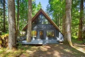 A-frame home with overhanging roof, a large deck and many trees around