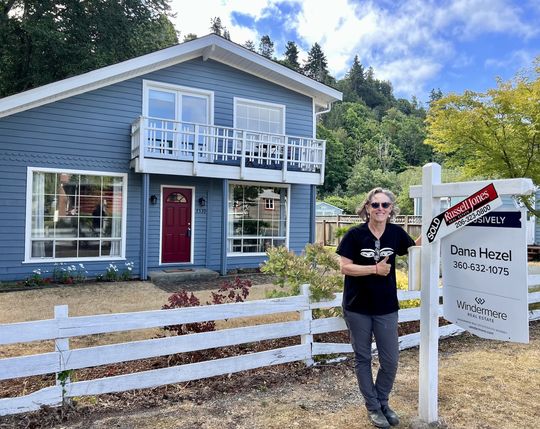 Jayn stands next to sold sign at 7539 Maxwelton Rd, Clinton, WA 98236