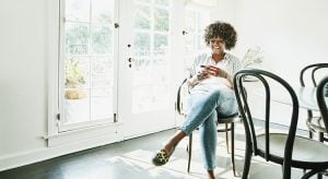 Smiling woman typing on smart phone while sitting in dining room