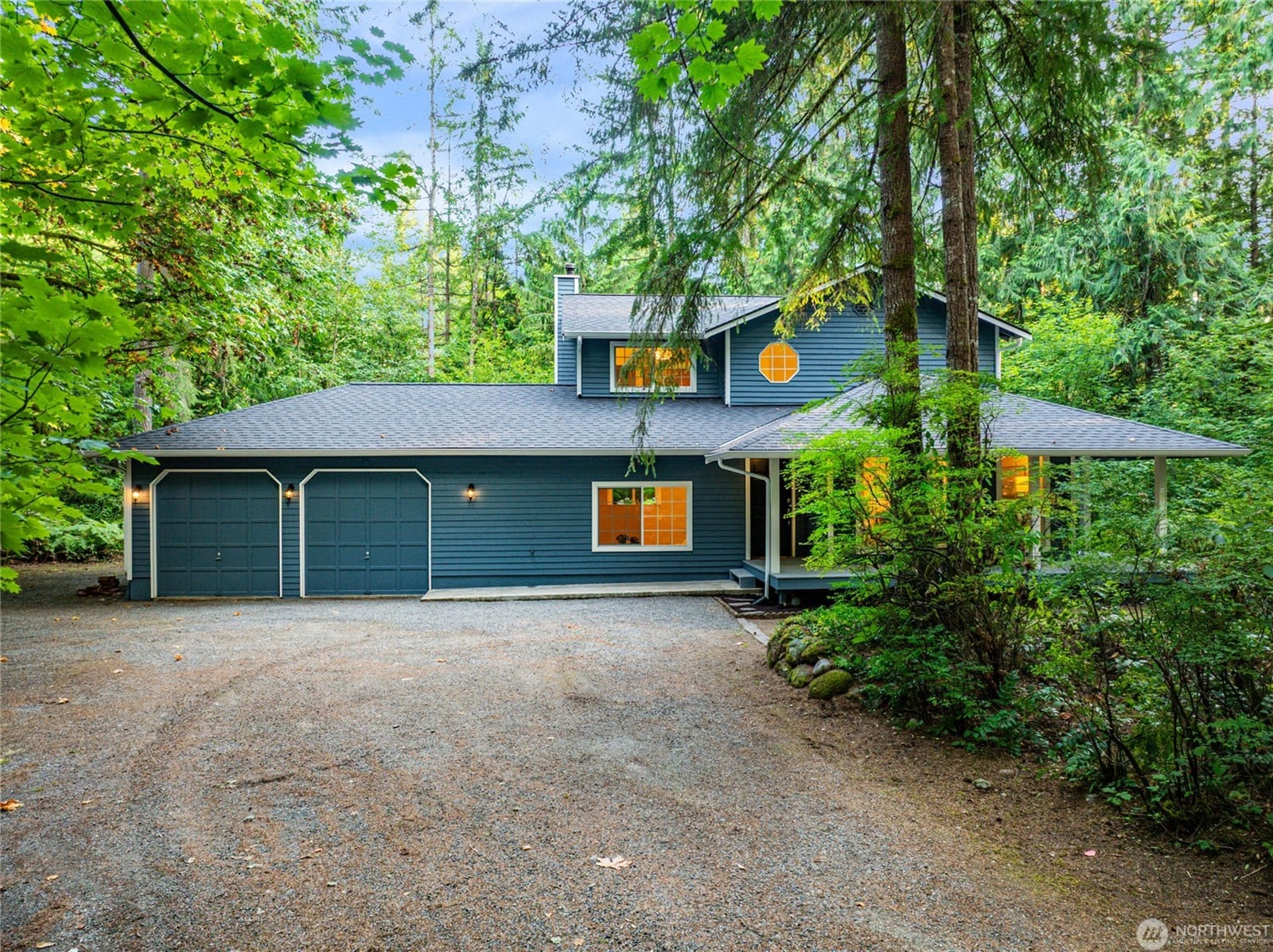 Blue two-story home with a covered porch and two-car garage set among tall evergreens in Carnation, WA