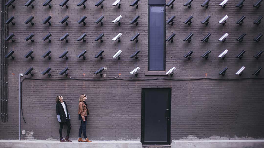 Video cameras mounted on a brick wall watching two women.