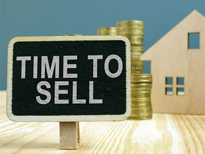 Time to sell your home graphic behind coins and a wooden house