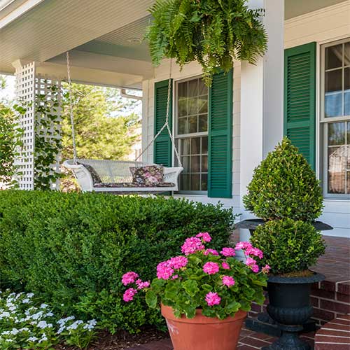 Front porch with pink flowers and green planters on steps and hanging by porch swing.