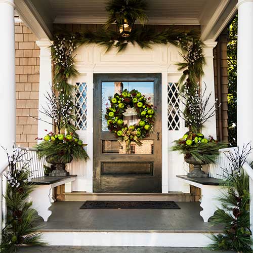 Wreath with apples and greenery hanging on a welcoming front porch door