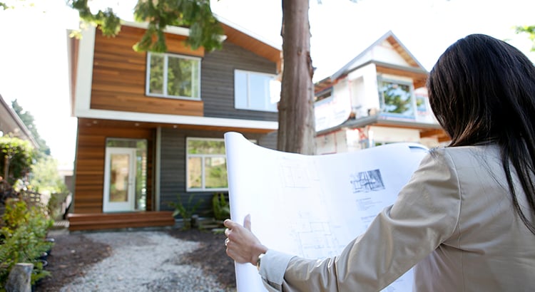 real estate agent standing near house reviewing blueprints