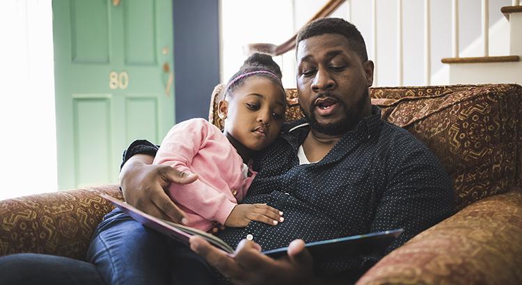 Father and daughter reading book in living room at home
