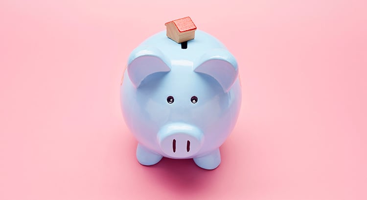 Still life of blue piggy bank and small house on pink background