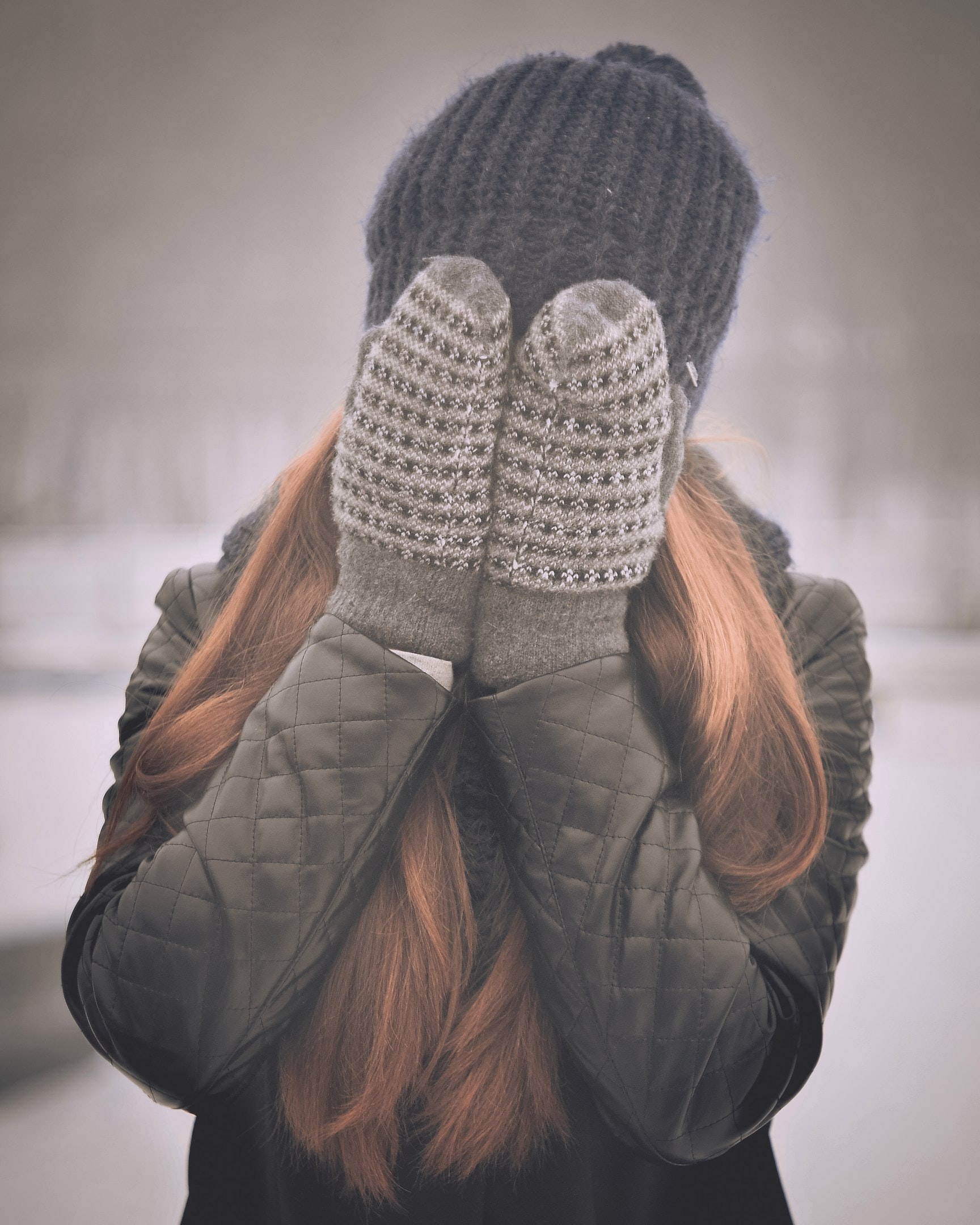 Woman covering her face with wool mittens