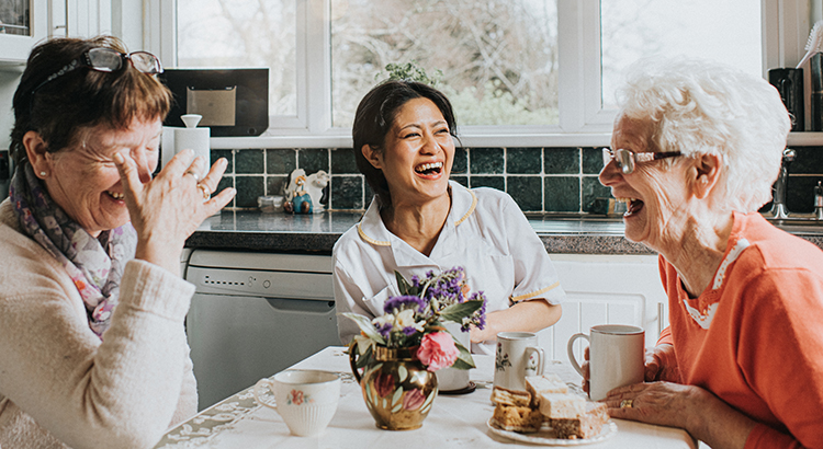 A carer laughs during a conversation with two older ladies at a kitchen table