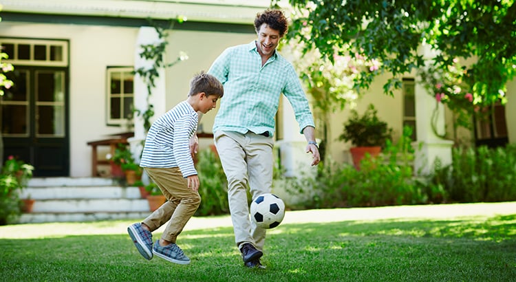Father and son playing soccer in lawn