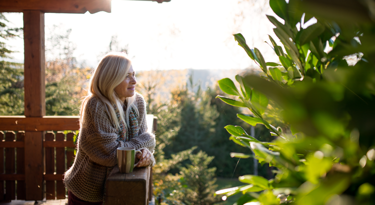 A woman drinking coffee on the deck while enjoying nature.