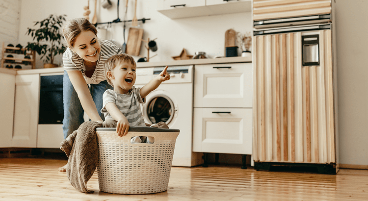 A mother playing with their son in a laundry basket.