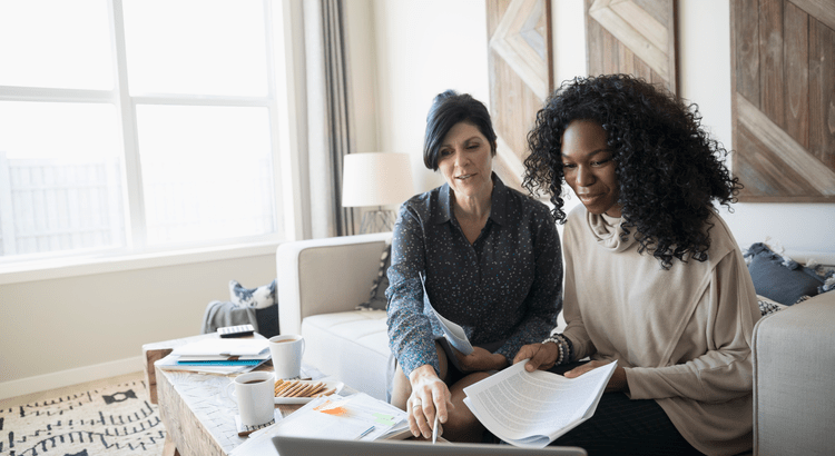 Two women reviewing a contract on the laptop in their living room.