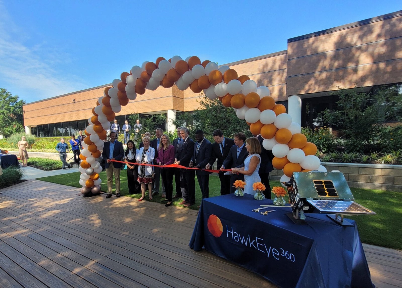 Ribbon cutting outside HawkEye 360 headquarters on Springpark Place in Herndon, with a satellite model on a HawkEye 360 table