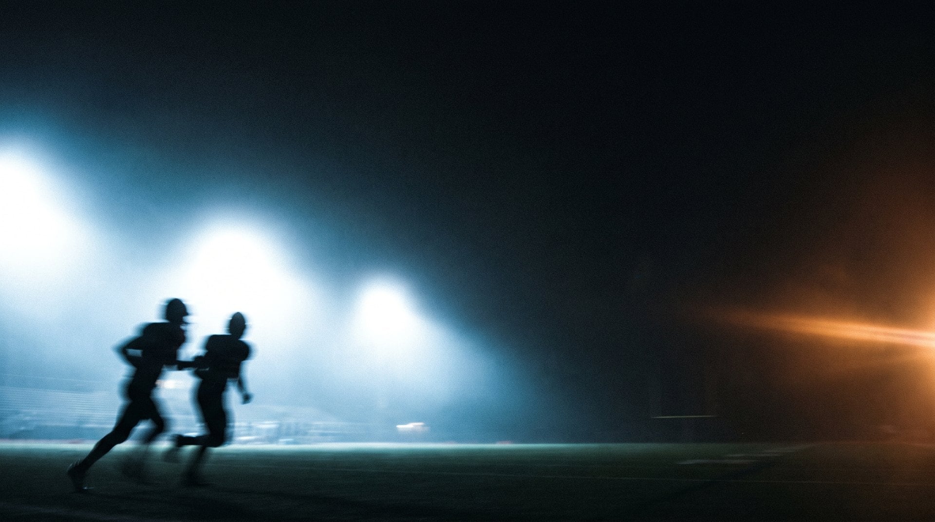 Backlit silhouettes of football players in motion under stadium lights at night