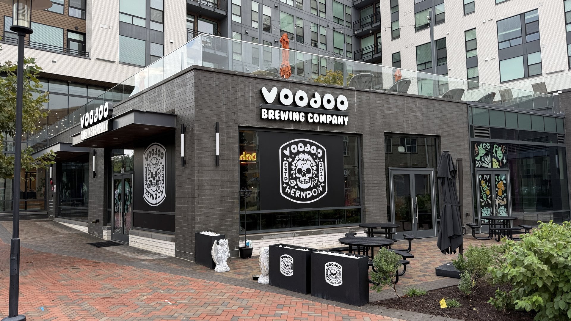 Exterior of Voodoo Brewing Company at Makers Rise on Dulles Station Boulevard in Herndon, Virginia, with its skull logo on the windows and patio tables out front