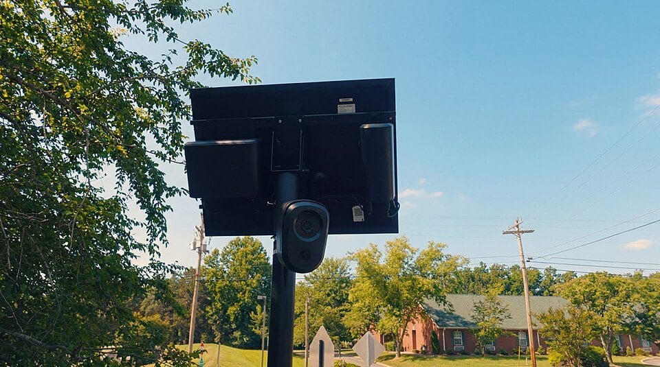 Flock license plate reader camera under a solar panel beside a residential street
