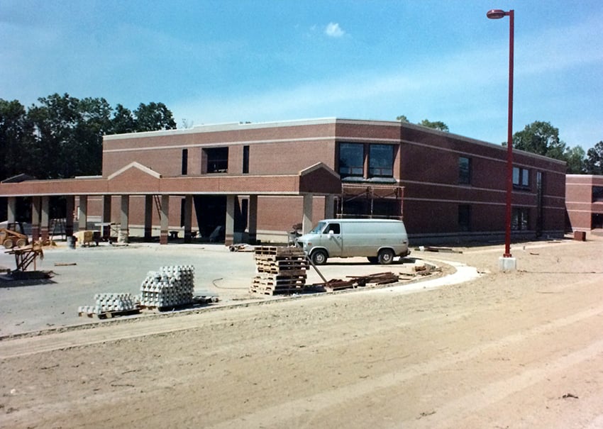 Aldrin Elementary School in Reston, Virginia, under construction in June 1993, a red brick two-story building with a covered entrance walkway, pallets of building materials and an unpaved front lot