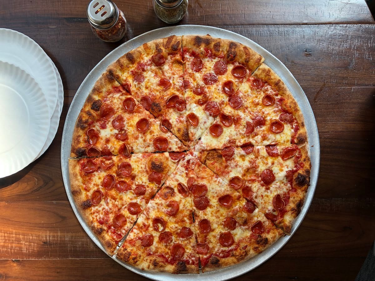 A whole New York-style pepperoni pizza from Andy's Pizza, cut into eight slices on a metal tray on a wooden table