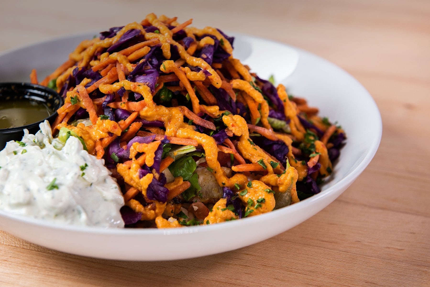 A Big Greek Bowl topped with shredded red cabbage, carrots and red pepper hummus, with tzatziki on the side