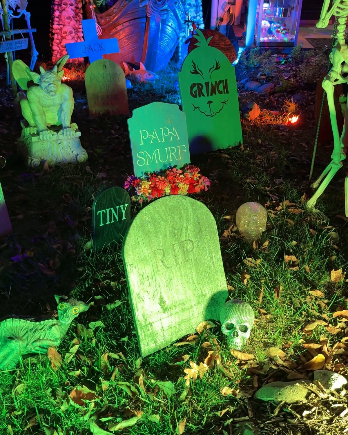 Tombstones lit green in the front-yard graveyard of the Historic Herndon Halloween House, including headstones for Papa Smurf and the Grinch