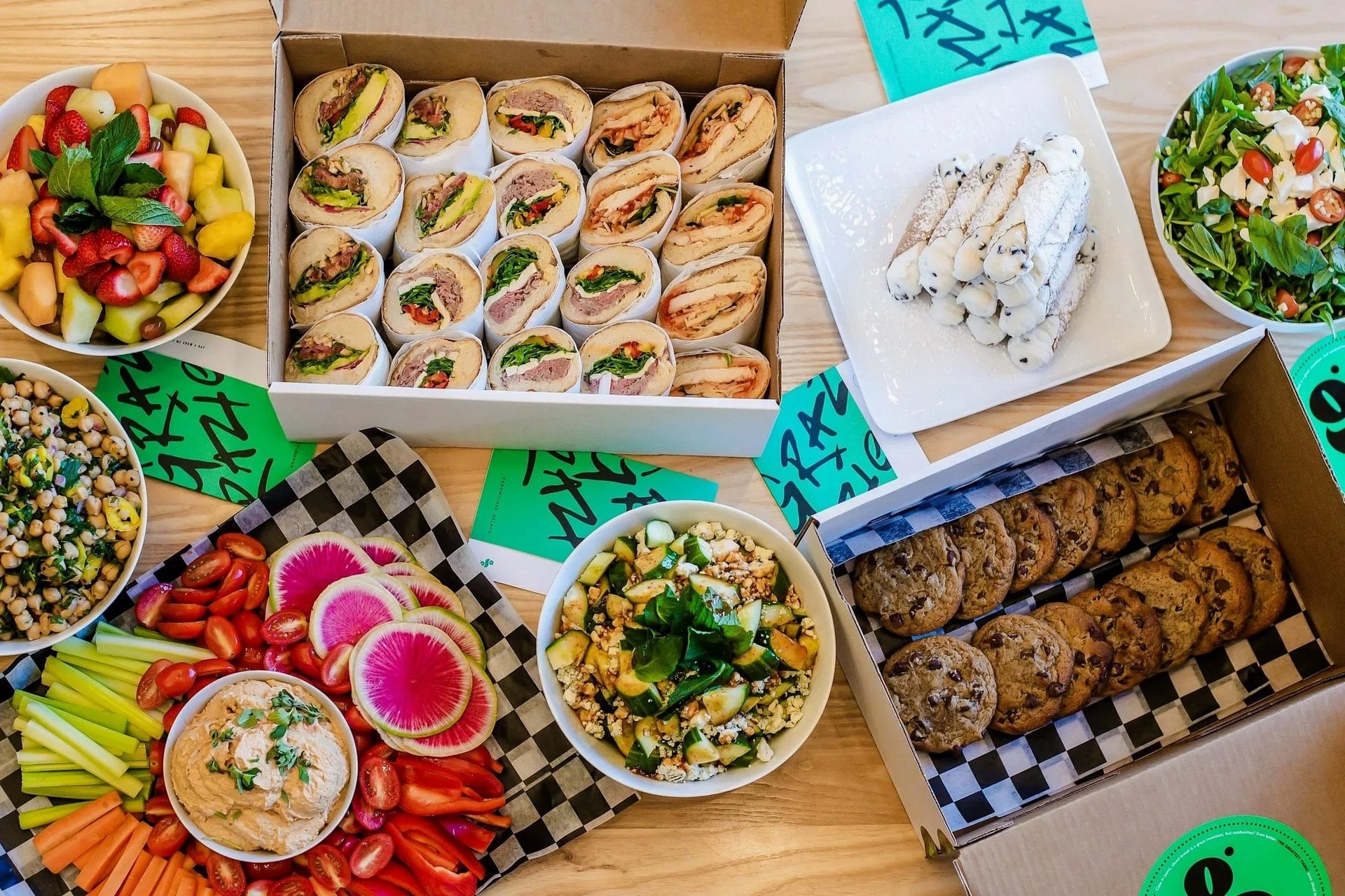 Overhead view of Grazie Grazie catering with a box of hoagie halves, cannoli, cookies, salads and crudites
