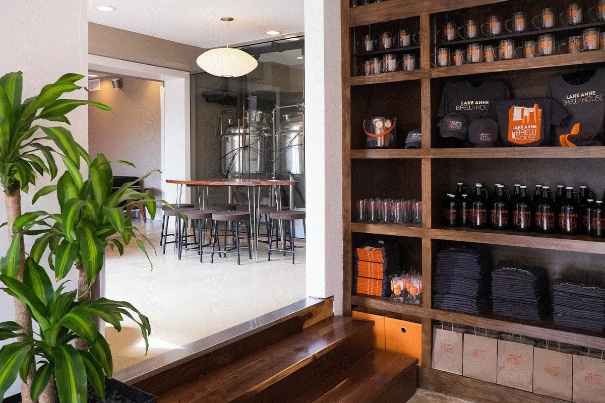 Inside Lake Anne Brew House at Lake Anne Plaza in Reston, with brewing tanks behind a seating area and shelves of growlers and merchandise