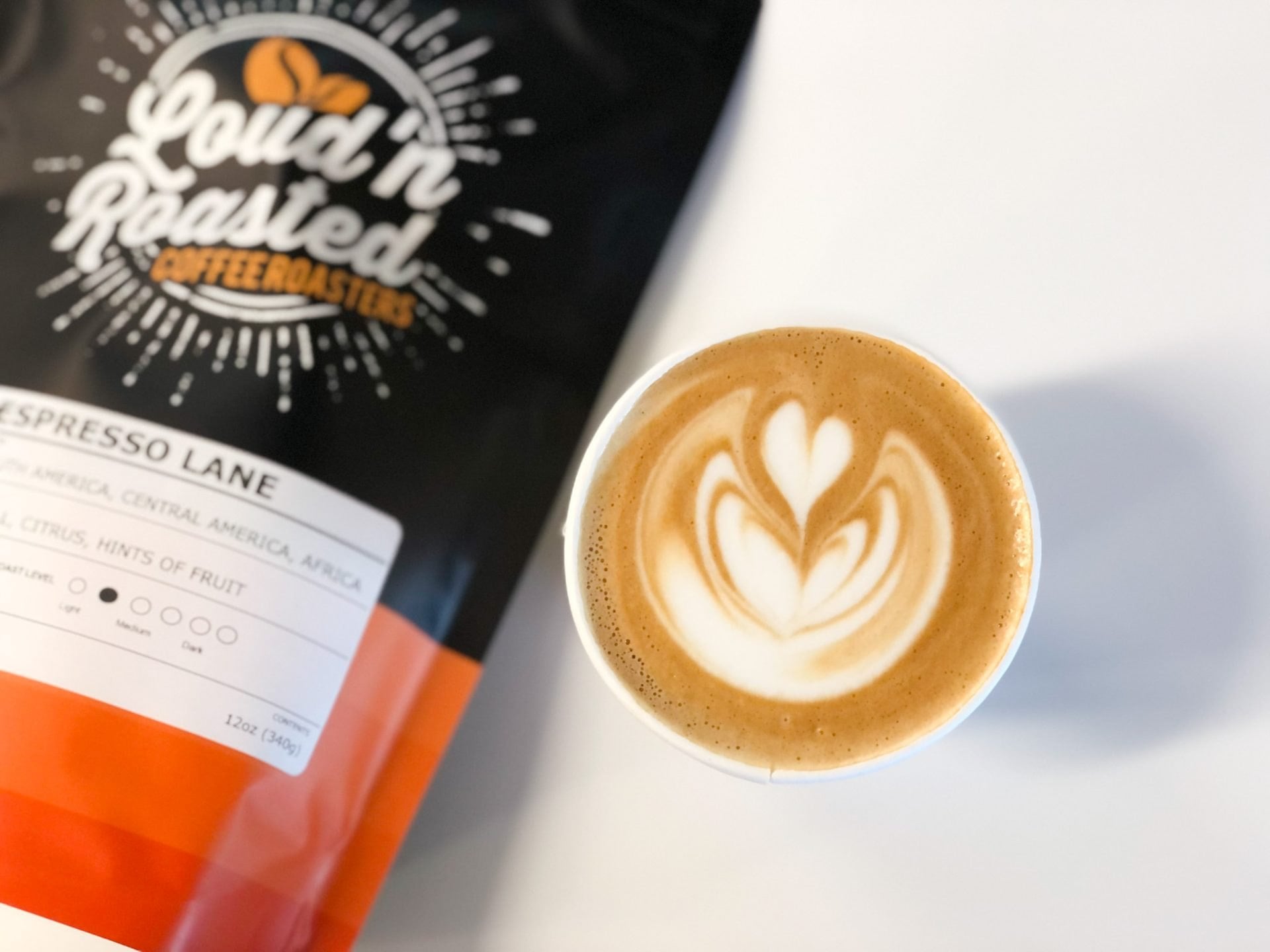 A bag of Loud'n Roasted Espresso Lane coffee beside a latte with heart latte art