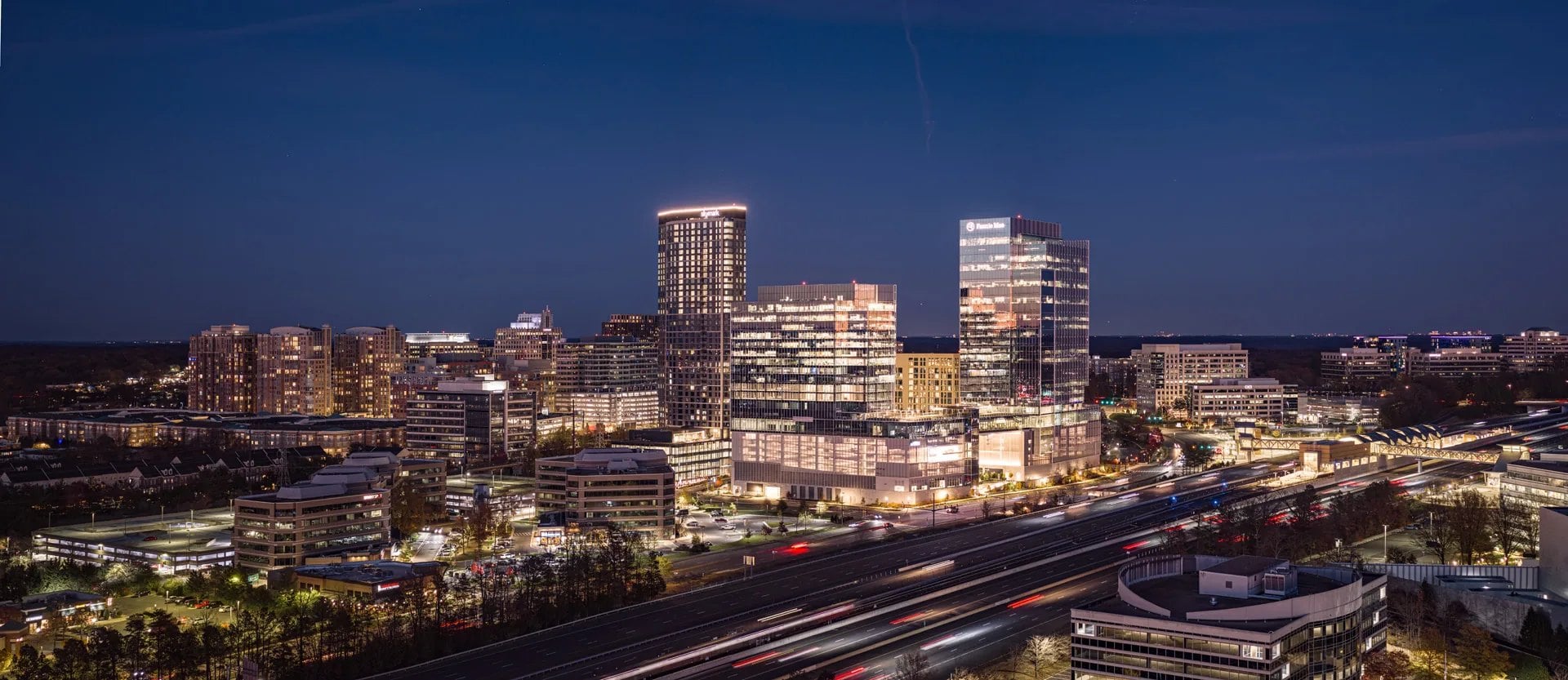 Reston Town Center office and apartment towers lit up at night beside the Dulles Toll Road