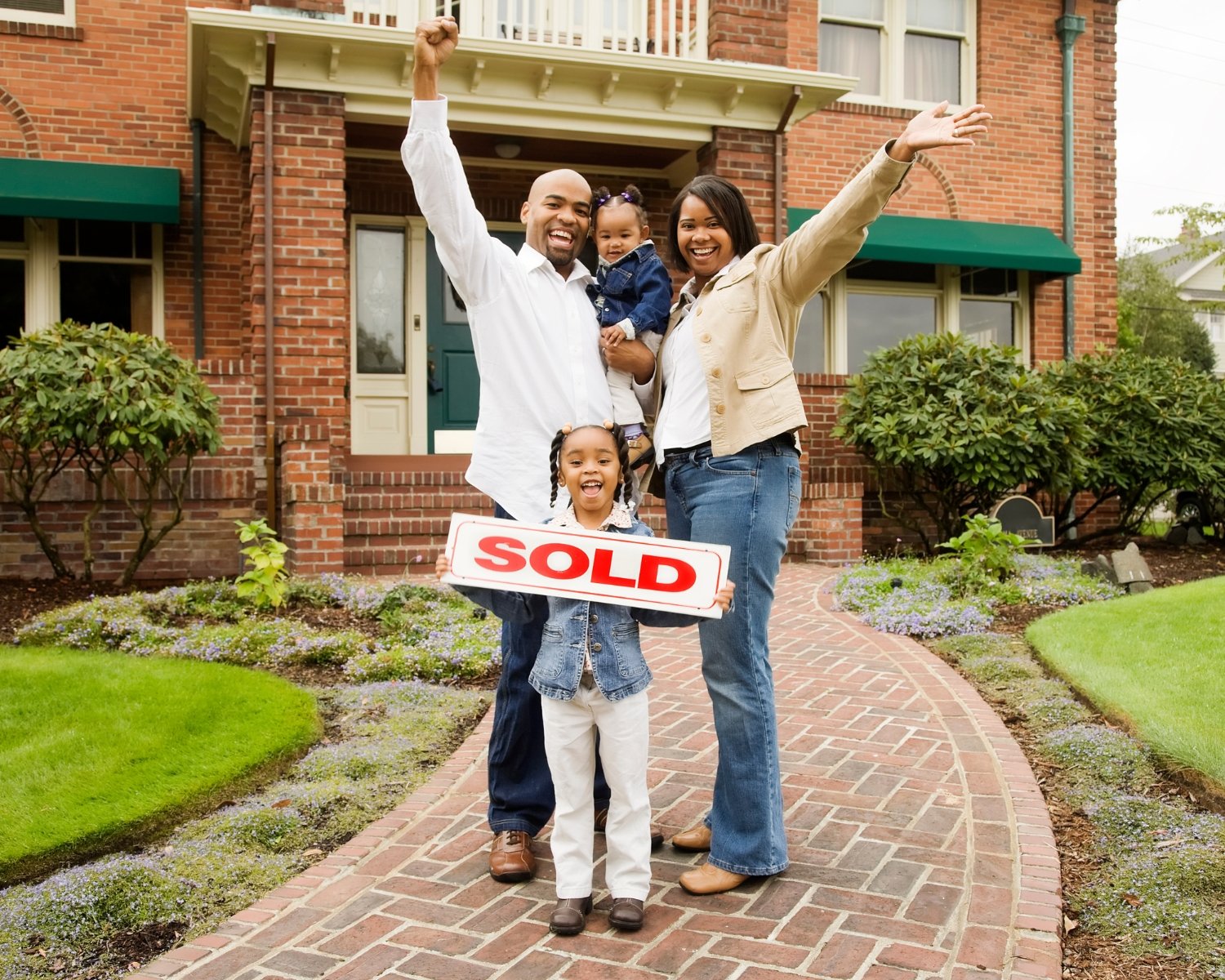 Family holding sold sign standing in front of beautiful home