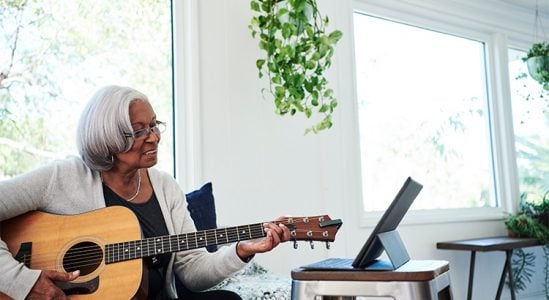 Senior woman playing guitar while facing laptop