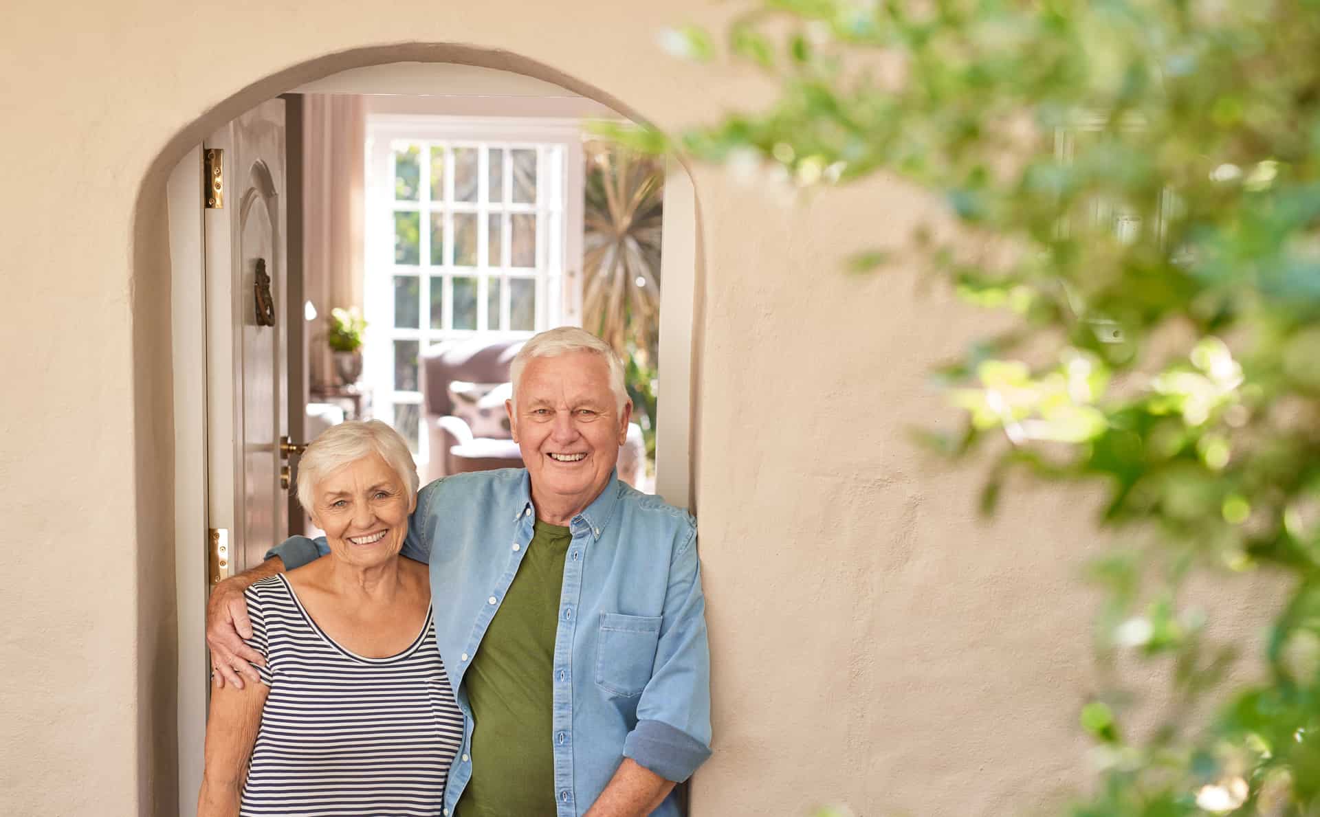 Happy senior couple smiling welcomingly at their front door