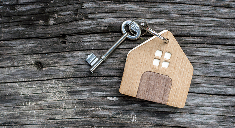 key with shaped house keychain on chain on wood texture background. Idea: buying a house, renting, selling real estate