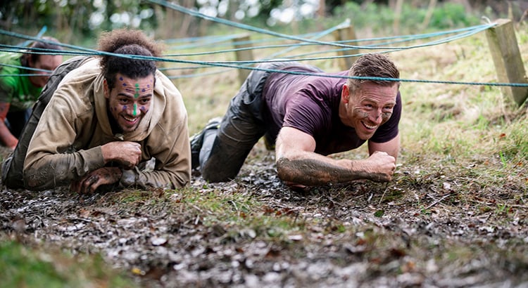Male friends crawling together in mud on outdoor obstacle course