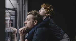 Father and son looking out of window on rainy day