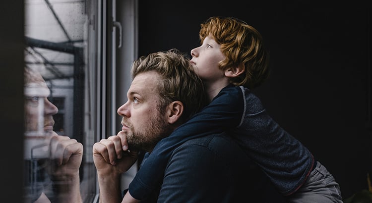 Father and son looking out of window on rainy day
