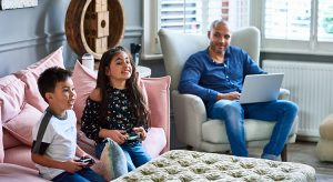 Father using laptop watching son and daughter play video game