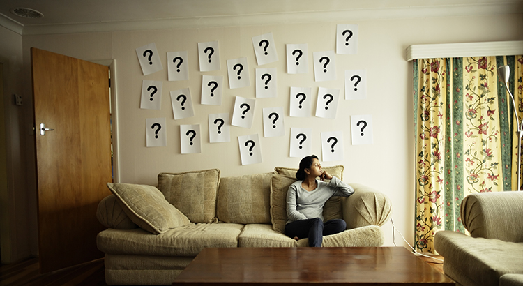 Woman sitting on sofa with question marks on wall.