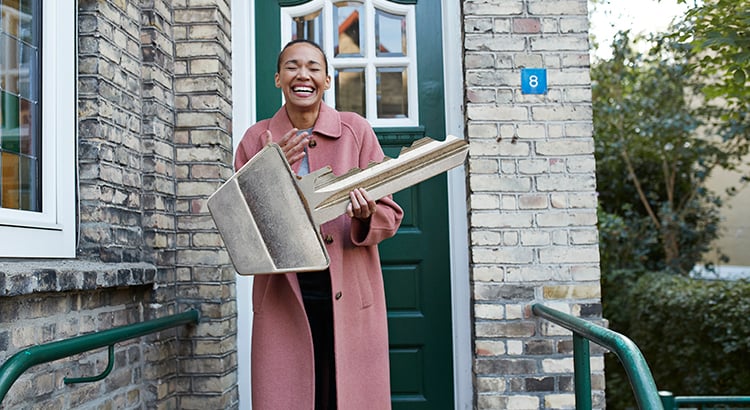 Cheerful young woman holding large key outside new house