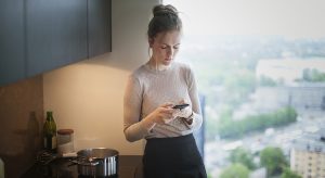 young woman in kitchen with smartphone