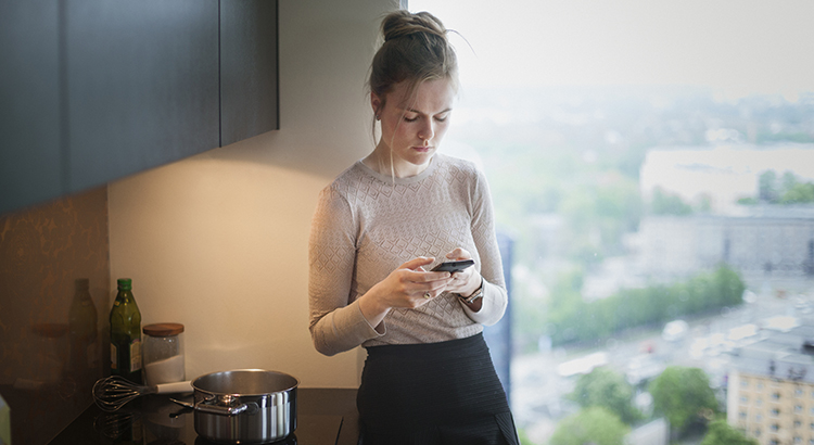 young woman in kitchen with smartphone