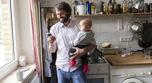 Father holding baby son while using smartphone.