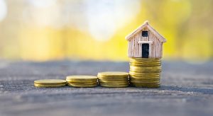 Coins stacks with a tiny toy house on top.