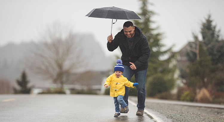 Father and toddler son walking together in the road while father is holding a umbrella