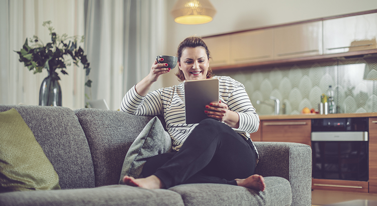 Young woman at home holding her tablet while sitting in sofa