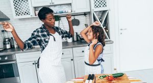 Mixed race mother and daughter dancing while cooking together in the kitchen