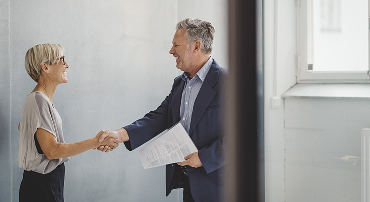 Mature businessman and businesswoman shaking hands in new office