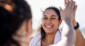 Smiling woman giving high five to her friend after exercising. Woman looking happy after a successful workout session outdoors.